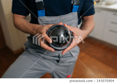 Technician in uniform holding dome surveillance camera. Close-up on hands installing home security system equipment. Concept of safety, protection, monitoring professional service. Technician in uniform holding dome surveillance camera. Close-up on hands installing home security system equipment. Concept of safety, protection, monitoring professional service. 143070904