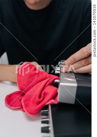 Close-up of male hands wiping dust from sound mixer with red microfiber cloth. Person adjusts silver knobs on professional audio interface. Concept of maintenance and care for technology. Close-up of male hands wiping dust from sound mixer with red microfiber cloth. Person adjusts silver knobs on professional audio interface. Concept of maintenance and care for technology. 143070938