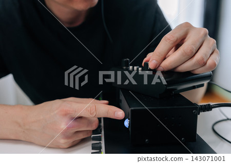 Person adjusting mixing console knobs and pushing buttons, creating and controlling sounds with various electronic music production devices in home recording studio. Person adjusting mixing console knobs and pushing buttons, creating and controlling sounds with various electronic music production devices in home recording studio. 143071001