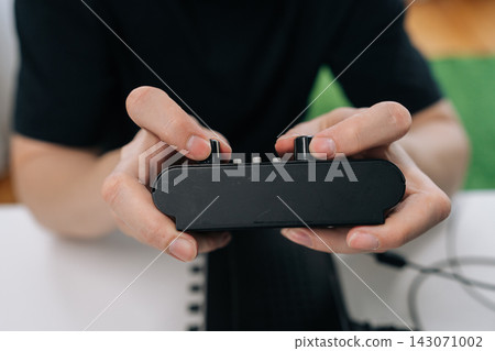 Person hands manipulating knobs and buttons on black audio electronics device, fine tuning settings for sound or music production in close-up view. 143071002