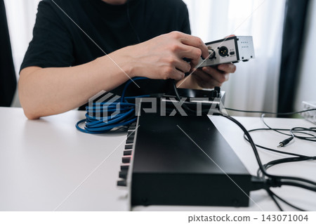 Person hands connecting audio interface to synthesizer or midi controller with xlr and jack cables, setting up home music studio for composing and recording sounds. Person hands connecting audio interface to synthesizer or midi controller with xlr and jack cables, setting up home music studio for composing and recording sounds. 143071004