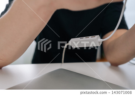 Close-up shot of person in black shirt at white desk holding multiport USB adapter. Shallow depth of field focuses on technology gadget. Modern, clean workspace concept for business or remote work. 143071008