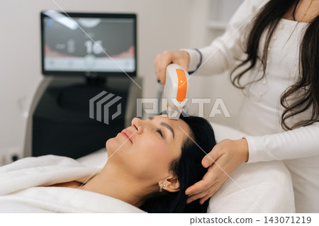 Relaxed middle-aged female receiving non invasive photorejuvenation laser therapy from cosmetologist for skin rejuvenation, facial lifting, antiaging wrinkle reduction treatment in beauty clinic. Relaxed middle-aged female receiving non invasive photorejuvenation laser therapy from cosmetologist for skin rejuvenation, facial lifting, antiaging wrinkle reduction treatment in beauty clinic. 143071219
