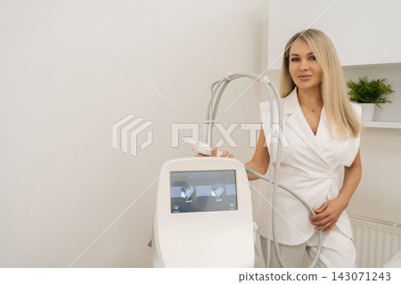 Cosmetologist female preparing microneedling machine for an anti aging radiofrequency skin treatment, selecting settings on touchscreen for a beauty procedure in clinic, looking at camera. Cosmetologist female preparing microneedling machine for an anti aging radiofrequency skin treatment, selecting settings on touchscreen for a beauty procedure in clinic, looking at camera. 143071243