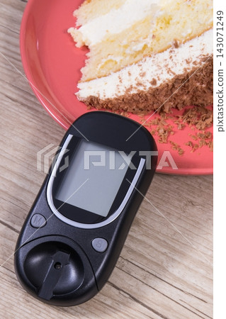Glucometer and sweet cake with chocolate. Measuring and checking sugar level during diabetes Glucometer and sweet cake with chocolate. Measuring and checking sugar level during diabetes 143071249