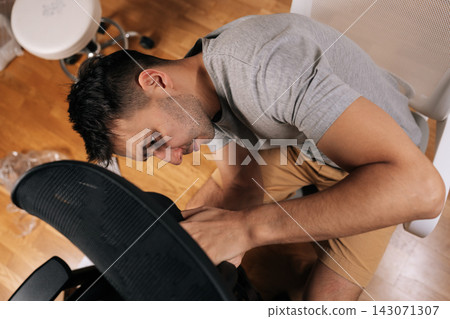 Top view of man assembling office chair at home, following instructions while feeling challenged and concentrated during diy furniture construction and home maintenance project. Top view of man assembling office chair at home, following instructions while feeling challenged and concentrated during diy furniture construction and home maintenance project. 143071307