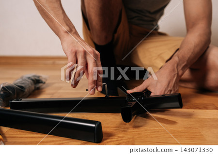 Master male assembling new office chair furniture, carefully using allen key to attach legs to central base while kneeling on wooden floor during home project. Master male assembling new office chair furniture, carefully using allen key to attach legs to central base while kneeling on wooden floor during home project. 143071330