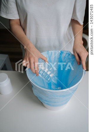 Person hands dropping multiple glass ampoules of expired medication into blue plastic garbage bag inside white trash can, illustrating proper and safe disposal of pharmaceutical waste. Person hands dropping multiple glass ampoules of expired medication into blue plastic garbage bag inside white trash can, illustrating proper and safe disposal of pharmaceutical waste. 143071485
