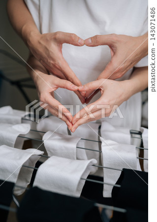 Close-up of couple forming heart gesture with hands over drying rack full of newly washed white and black socks, symbolizing shared domestic chores, teamwork, love, partnership in daily life. Close-up of couple forming heart gesture with hands over drying rack full of newly washed white and black socks, symbolizing shared domestic chores, teamwork, love, partnership in daily life. 143071486