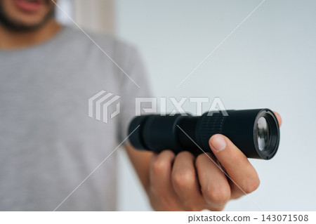 Close-up hands of unrecognizable person holding black monocular in hand, extending forward, focusing with optical instrument to observe something unseen. Concept of discovering, exploring, vision. 143071508