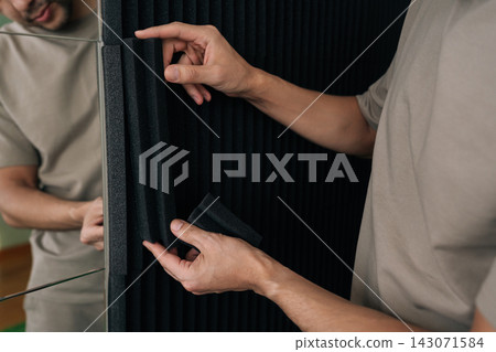 Person installing black acoustic foam soundproof panels on a wall, enhancing sound insulation and improving room acoustics for recording studios or home theaters. Person installing black acoustic foam soundproof panels on a wall, enhancing sound insulation and improving room acoustics for recording studios or home theaters. 143071584