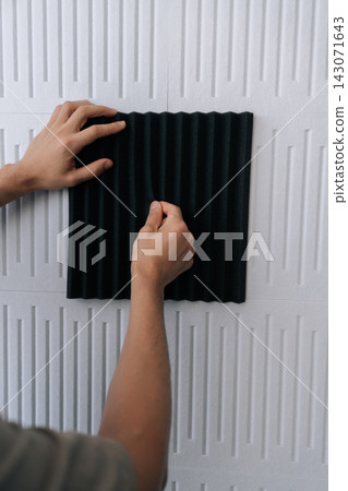 Vertical cropped shot of craftsman installing black acoustic foam panel on white decorative wall to reduce echo, improve sound quality in a home studio or recording space during renovation project. Vertical cropped shot of craftsman installing black acoustic foam panel on white decorative wall to reduce echo, improve sound quality in a home studio or recording space during renovation project. 143071643