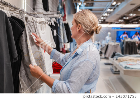 Woman Browsing Clothing Rack in Modern Fashion Store Woman Browsing Clothing Rack in Modern Fashion Store 143071753