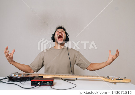 Excited guitarist passionately expressing emotional intensity, recording music with bass guitar through audio interface and headphones, capturing sound in home studio environment, isolated background. Excited guitarist passionately expressing emotional intensity, recording music with bass guitar through audio interface and headphones, capturing sound in home studio environment, isolated background. 143071815