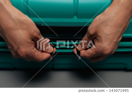 Two hands zipping a turquoise suitcase, preparing for a trip, packing luggage, or unpacking after travel, symbolizing journey, adventure, and personal belonging management. Two hands zipping a turquoise suitcase, preparing for a trip, packing luggage, or unpacking after travel, symbolizing journey, adventure, and personal belonging management. 143071995