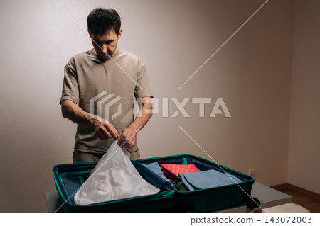 Portrait of traveler young man organizing baggage, packing shoes into a protective bag inside a luggage, preparing for an exciting journey, departure, or vacation. 143072003