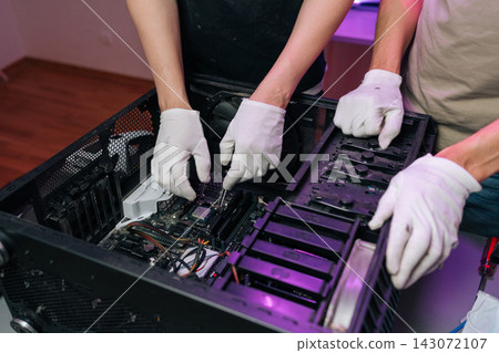 Close-up of two people in white gloves working together on computer hardware. Technicians installing CPU on motherboard. Concept of PC assembly, repair service, teamwork technology. Close-up of two people in white gloves working together on computer hardware. Technicians installing CPU on motherboard. Concept of PC assembly, repair service, teamwork technology. 143072107