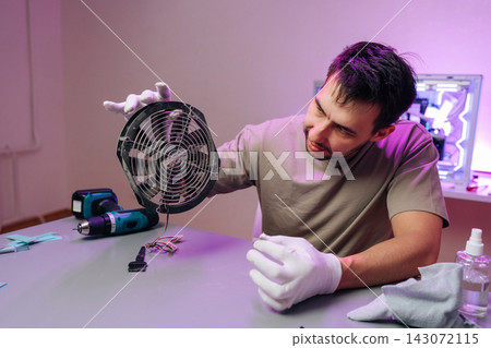 Technician in white gloves holding dusty CPU cooling fan removed from pc chassis, inspecting and preparing hardware for cleaning and maintenance in workshop setting. Technician in white gloves holding dusty CPU cooling fan removed from pc chassis, inspecting and preparing hardware for cleaning and maintenance in workshop setting. 143072115