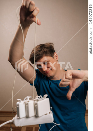 Vertical shot of person frustrated by tangled power cords and multiple chargers connected to an overloaded power strip, giving thumbs down gesture expressing dissatisfaction with technology issues. Vertical shot of person frustrated by tangled power cords and multiple chargers connected to an overloaded power strip, giving thumbs down gesture expressing dissatisfaction with technology issues. 143072216