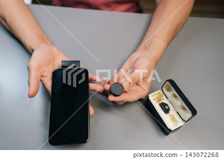 Broadcaster connecting wireless lapel microphone system with lightning adapter to modern smartphone, demonstrating setup for mobile audio recording or vlogging, close-up, cropped shot. Broadcaster connecting wireless lapel microphone system with lightning adapter to modern smartphone, demonstrating setup for mobile audio recording or vlogging, close-up, cropped shot. 143072268