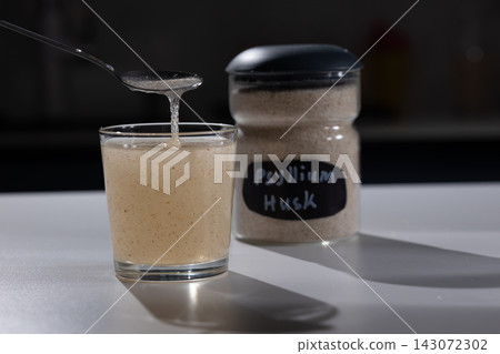 Soaked psyllium husk gel drips from a spoon into a glass on a kitchen counter Soaked psyllium husk gel drips from a spoon into a glass on a kitchen counter 143072302
