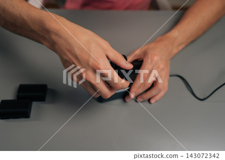 Top view of person placing red lithium-ion battery into dual-slot digital camera charger on gray table, actively powering up essential photography gear for creative work. Top view of person placing red lithium-ion battery into dual-slot digital camera charger on gray table, actively powering up essential photography gear for creative work. 143072342