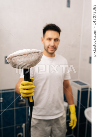 Vertical shot of man in yellow gloves holding active steam cleaner, cleaning surfaces in modern bathroom, focusing on eco-friendly sanitation and maintaining spotless home environment. Vertical shot of man in yellow gloves holding active steam cleaner, cleaning surfaces in modern bathroom, focusing on eco-friendly sanitation and maintaining spotless home environment. 143072365