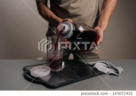 Man pouring refreshing homemade red berry fruit compote into glass from clear carafe, serving healthy sugar-free beverage, natural refreshing drink, close-up, cropped shot. Man pouring refreshing homemade red berry fruit compote into glass from clear carafe, serving healthy sugar-free beverage, natural refreshing drink, close-up, cropped shot. 143072425
