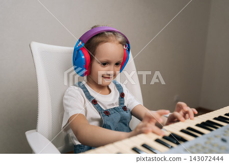 Young girl with colorful headphones enjoying hobby, playing an electronic keyboard, developing creativity and musical talent while focusing on lesson or practicing at home. Young girl with colorful headphones enjoying hobby, playing an electronic keyboard, developing creativity and musical talent while focusing on lesson or practicing at home. 143072444