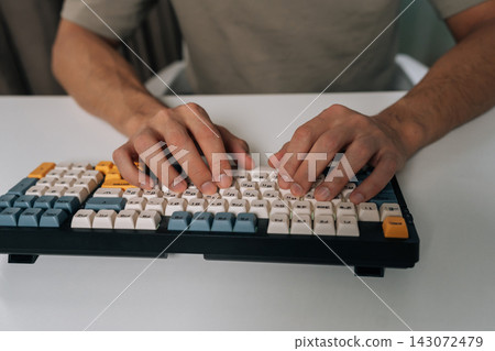 Close-up of person hands typing on stylish wireless mechanical keyboard with colored keycaps, demonstrating efficient digital work, productivity and modern technology use in home office environment. Close-up of person hands typing on stylish wireless mechanical keyboard with colored keycaps, demonstrating efficient digital work, productivity and modern technology use in home office environment. 143072479
