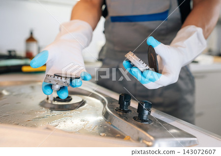 Close-up of professional cleaner hands in rubber gloves disassembling dirty gas hob for deep cleaning. Focus on appliance maintenance and domestic hygiene service. Bright, clean lighting. Close-up of professional cleaner hands in rubber gloves disassembling dirty gas hob for deep cleaning. Focus on appliance maintenance and domestic hygiene service. Bright, clean lighting. 143072607