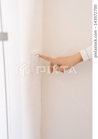 Person hand pushing white light switch mounted on textured wall, managing power for illumination and energy conservation in minimalist indoor setting. 143072700