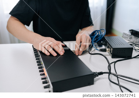 Close-up of hands plugging blue audio jack into sound mixer. Represents music production, sound engineering, or podcasting in studio setting with professional equipment on white table. Close-up of hands plugging blue audio jack into sound mixer. Represents music production, sound engineering, or podcasting in studio setting with professional equipment on white table. 143072741