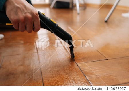 Cleaning service employee sanitizing floor with a steam machine, maintaining household cleanliness and effectively eliminating grime from tiled surface with hot steam. Concept of domestic hygiene. Cleaning service employee sanitizing floor with a steam machine, maintaining household cleanliness and effectively eliminating grime from tiled surface with hot steam. Concept of domestic hygiene. 143072927