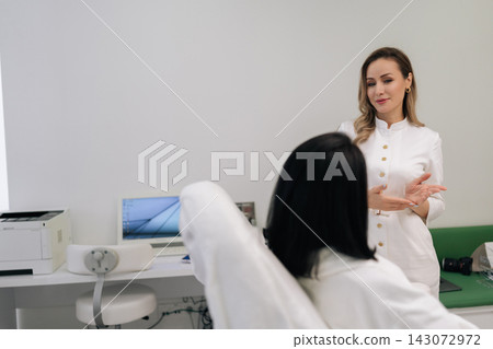 Portrait of aesthetician doctor discussing beauty procedure with female client sitting in chair in modern aesthetic medicine clinic, explaining details of treatment during consultation. Portrait of aesthetician doctor discussing beauty procedure with female client sitting in chair in modern aesthetic medicine clinic, explaining details of treatment during consultation. 143072972