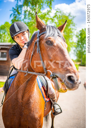 Lovely young woman wearing helmet riding her brown horse 143072975