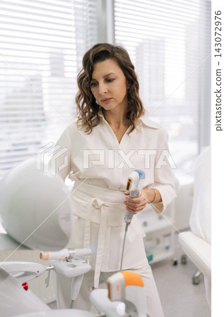 Vertical portrait of cosmetologist preparing ultrasound lifting device, adjusting settings for facial skin tightening treatment in modern beauty clinic, providing effective anti-aging therapy. Vertical portrait of cosmetologist preparing ultrasound lifting device, adjusting settings for facial skin tightening treatment in modern beauty clinic, providing effective anti-aging therapy. 143072976
