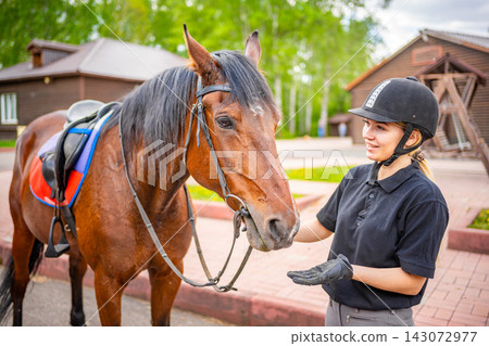 Lovely young woman wearing helmet stroking to her brown horse Lovely young woman wearing helmet stroking to her brown horse 143072977