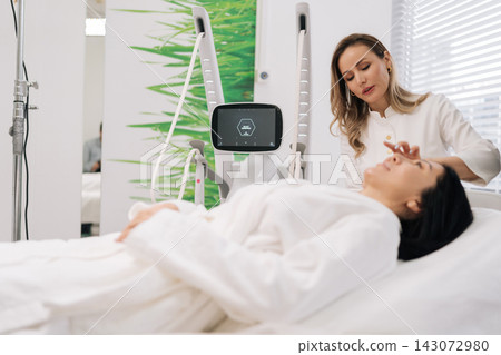 Female cosmetologist performing microneedling mesotherapy treatment on female client face, focusing on skin rejuvenation, anti-aging, aesthetic care in beauty clinic. Concept of healthy lifestyle. Female cosmetologist performing microneedling mesotherapy treatment on female client face, focusing on skin rejuvenation, anti-aging, aesthetic care in beauty clinic. Concept of healthy lifestyle. 143072980