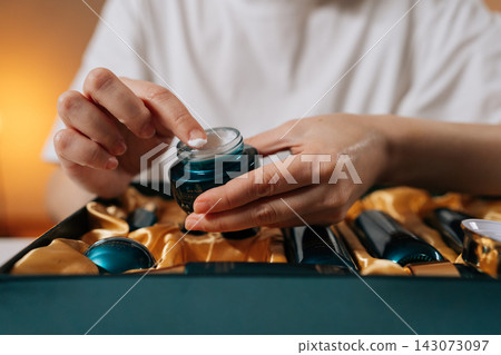 Closeup of woman opening luxurious facial cream jar from premium skincare gift set, scooping rich moisturizer onto fingertip in close-up, symbolizing daily self-care, hydration and youthful glow. Closeup of woman opening luxurious facial cream jar from premium skincare gift set, scooping rich moisturizer onto fingertip in close-up, symbolizing daily self-care, hydration and youthful glow. 143073097