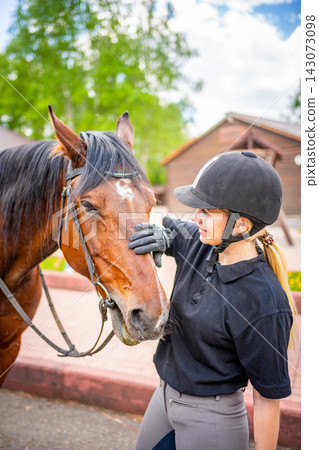 Lovely young woman wearing helmet stroking to her brown horse Lovely young woman wearing helmet stroking to her brown horse 143073098