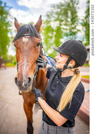 Lovely young woman wearing helmet stroking to her brown horse Lovely young woman wearing helmet stroking to her brown horse 143073102
