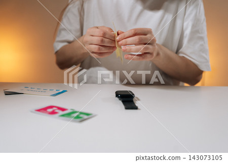 Female hands peeling back protective film layer, preparing to apply it to black smartwatch resting on white table, focusing on technology protection and device maintenance, close-up. Female hands peeling back protective film layer, preparing to apply it to black smartwatch resting on white table, focusing on technology protection and device maintenance, close-up. 143073105
