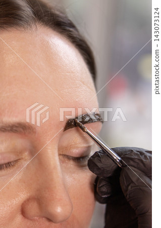Close up of eyebrow lamination treatment application by gloved hand with metal applicator Close up of eyebrow lamination treatment application by gloved hand with metal applicator 143073124