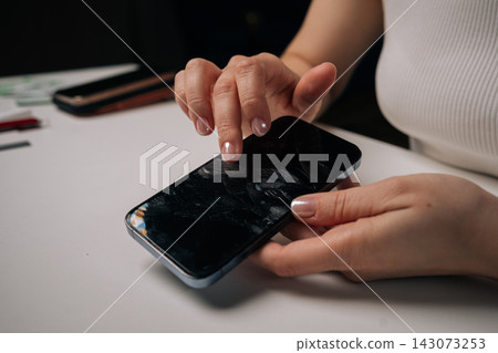 Woman peeling damaged screen protector from smartphone, exposing cracked protective film on white surface, revealing device compromised condition. Concept of mobile phone maintenance and service. Woman peeling damaged screen protector from smartphone, exposing cracked protective film on white surface, revealing device compromised condition. Concept of mobile phone maintenance and service. 143073253