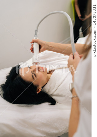 Vertical cropped shot of professional cosmetologist performing microneedle rf face lifting treatment on middle-aged woman cheek for skin tightening, rejuvenation, antiaging care in beauty clinic. Vertical cropped shot of professional cosmetologist performing microneedle rf face lifting treatment on middle-aged woman cheek for skin tightening, rejuvenation, antiaging care in beauty clinic. 143073331