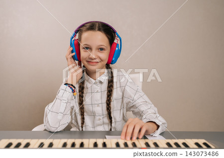 Cheerful young girl with braids wearing colorful headphones, focused and smiling playing digital piano, developing musical skills, concentration, enjoying creative hobby. Cheerful young girl with braids wearing colorful headphones, focused and smiling playing digital piano, developing musical skills, concentration, enjoying creative hobby. 143073486