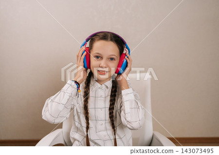 Young girl with pigtails holding colorful headphones on ears, happily engaging with audio entertainment, representing childhood leisure, learning, and digital enjoyment. Young girl with pigtails holding colorful headphones on ears, happily engaging with audio entertainment, representing childhood leisure, learning, and digital enjoyment. 143073495