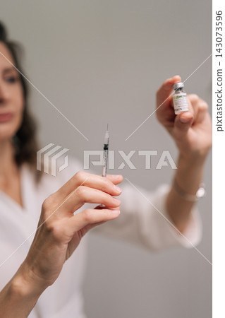 Vertical cropped shot of beautician filling syringe with medication from vial, preparing for beauty procedure in clinic of aesthetic medicine. Concept of beauty, facial anti-aging, skin care treatment Vertical cropped shot of beautician filling syringe with medication from vial, preparing for beauty procedure in clinic of aesthetic medicine. Concept of beauty, facial anti-aging, skin care treatment 143073596