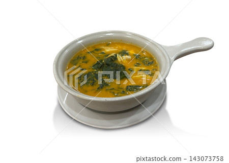 top view cassia leaf curry with crab meat in a handled ceramic bowl, placed on a ceramic tray against a white background. 143073758